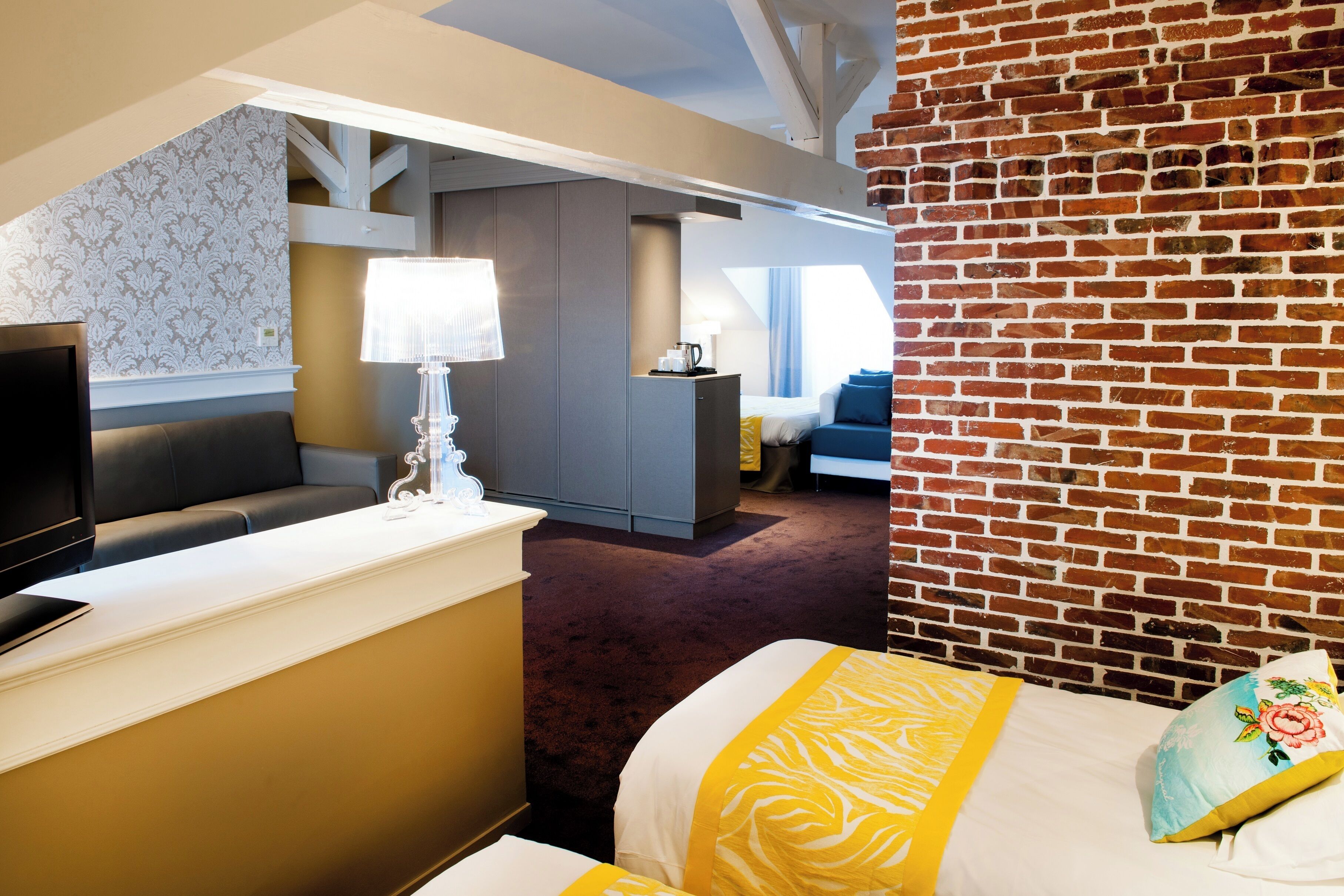 A hotel room with a bed, a desk, a television, and a brick wall.