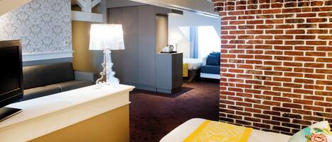 A hotel room with a bed, a desk, a television, and a brick wall.