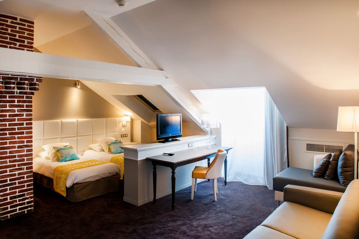 Ein Hotelzimmer mit einer Erkeretage, einem Schreibtisch mit Fernseher und einer Sitzecke inklusive Sofa und Sesseln.