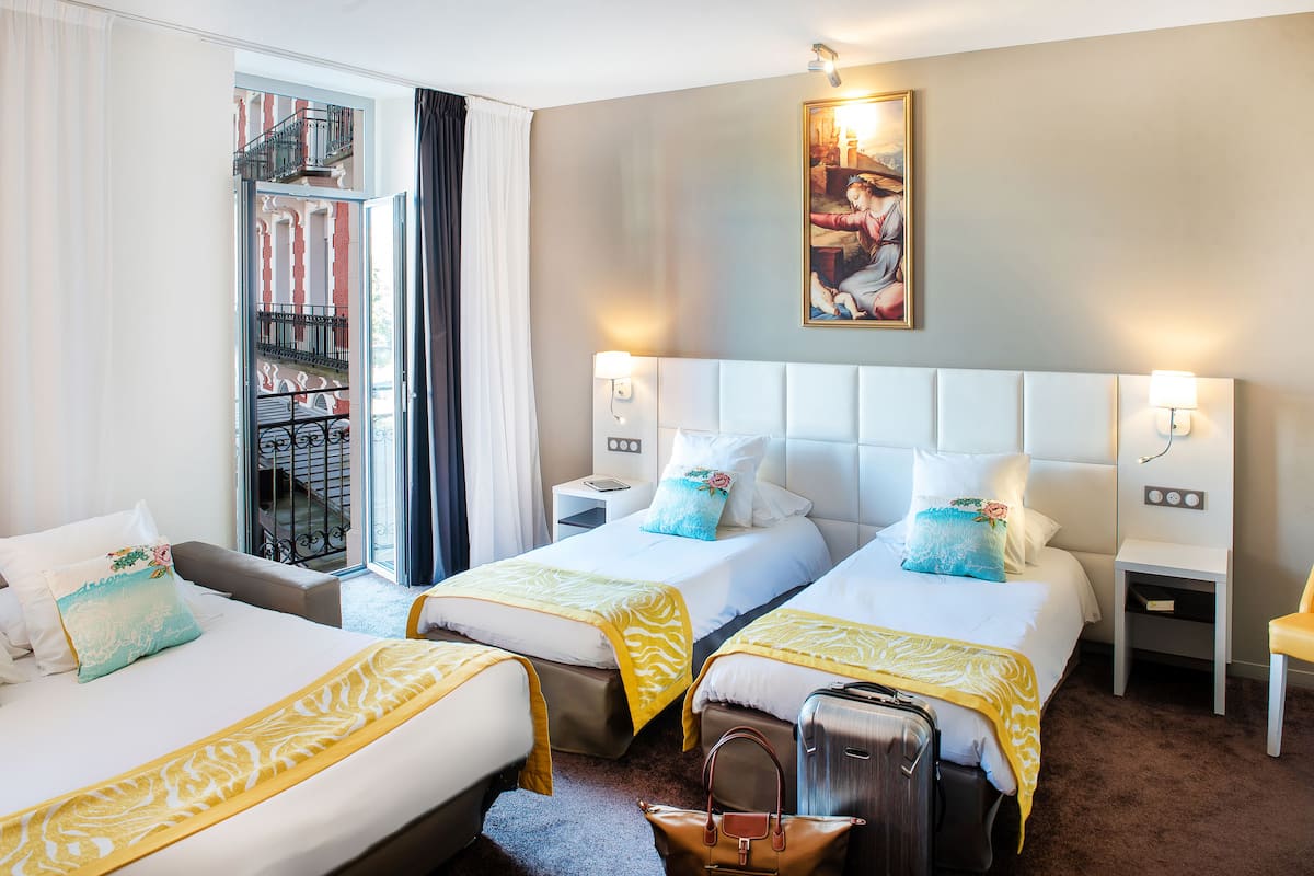 Ein Hotelzimmer mit zwei Betten, einer Sitzecke, einem Balkon mit Geländer und einem Bild an der Wand.