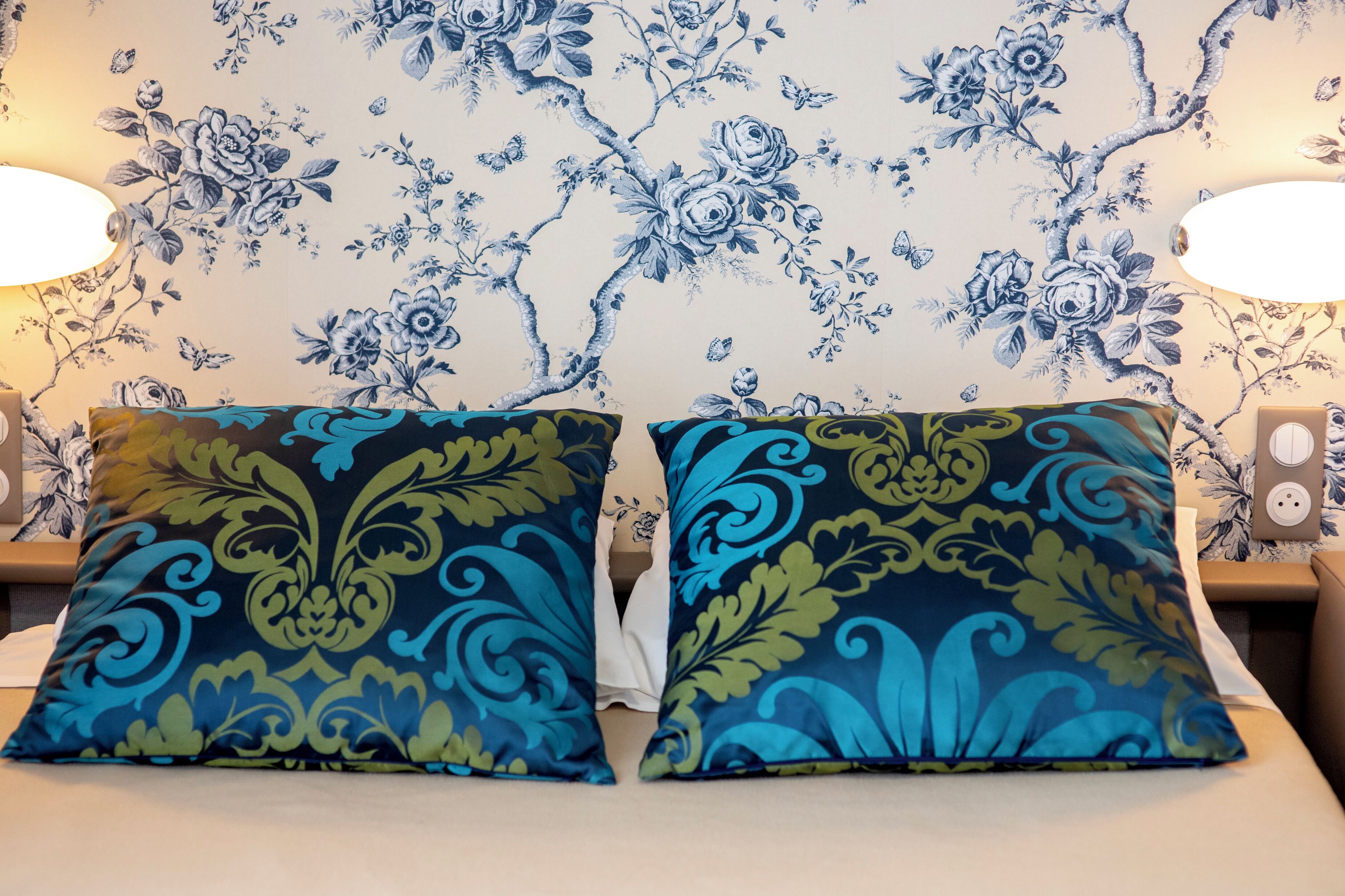 Una cama con dos almohadones decorativos y un estampado floral en el papel tapiz.