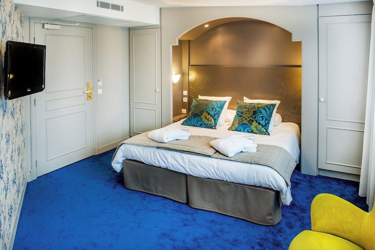 Ein Hotelzimmer mit einem großen Bett, einem an der Wand montierten Flachbildfernseher und einem blauen Teppich.