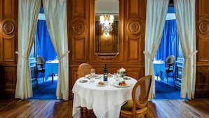 A dining room with a round table set for two, a chandelier, and a mirror above the table. - Grand Hotel Gallia & Londres (Lourdes)