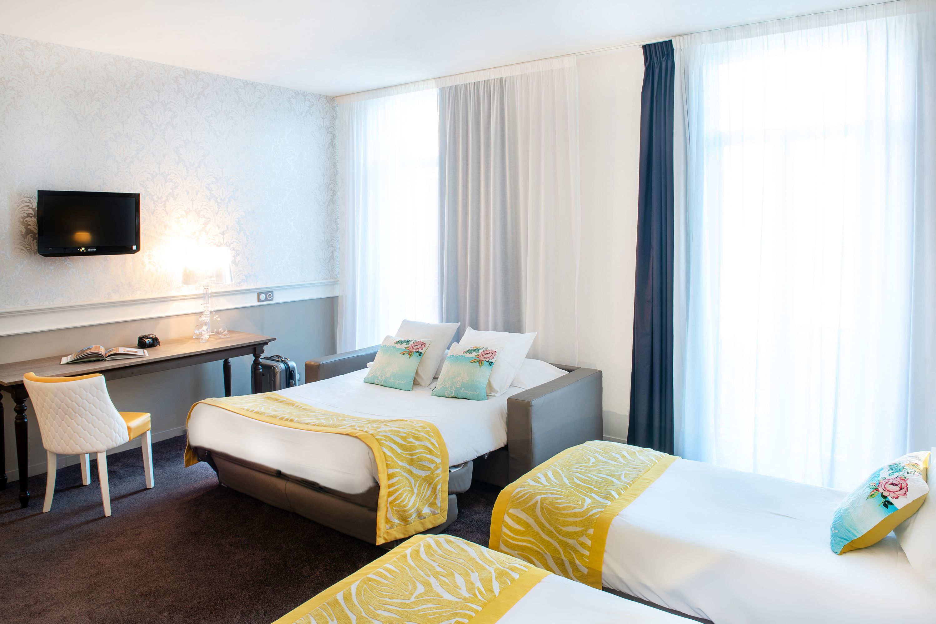 A hotel room with a bed, two bedside tables, a desk, a chair, and a flat-screen TV mounted on the wall.