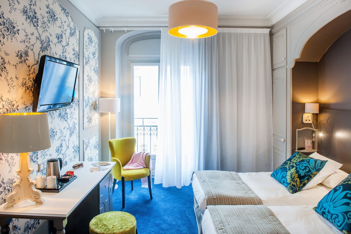 Ein Hotelzimmer mit Bett, Schreibtisch mit Lampe, Stuhl, Fernseher und einem Fenster mit Vorhängen.