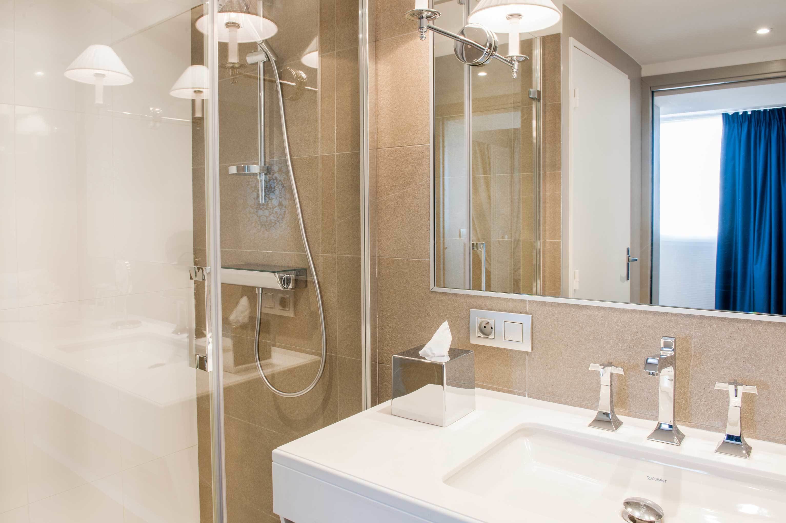 A modern bathroom with a glass-enclosed shower, a white sink with three faucets, and a large mirror.