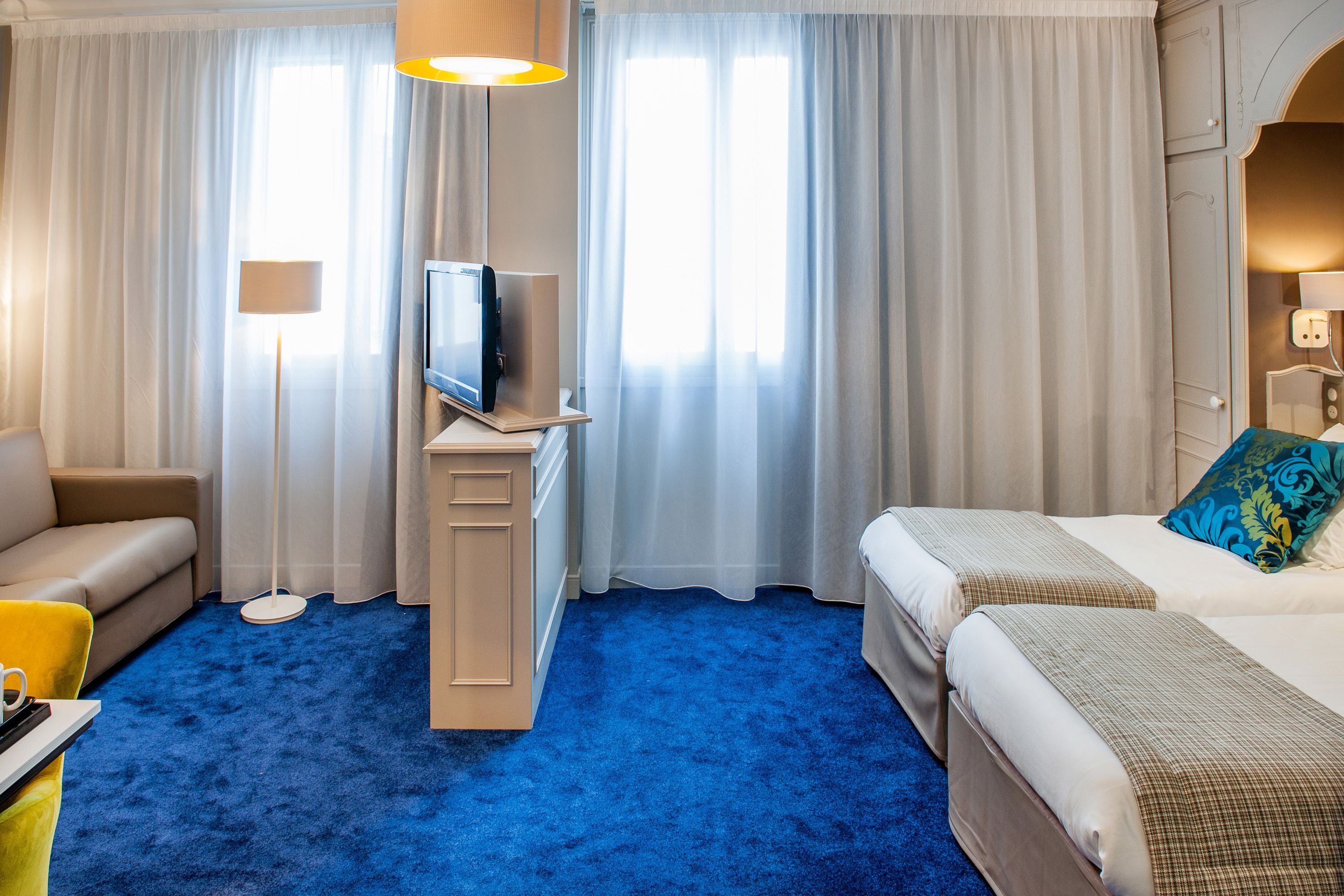 Ett hotellrum med ett blått golv, en soffa, en säng med en blå kudde och en tv som står på ett stativ.