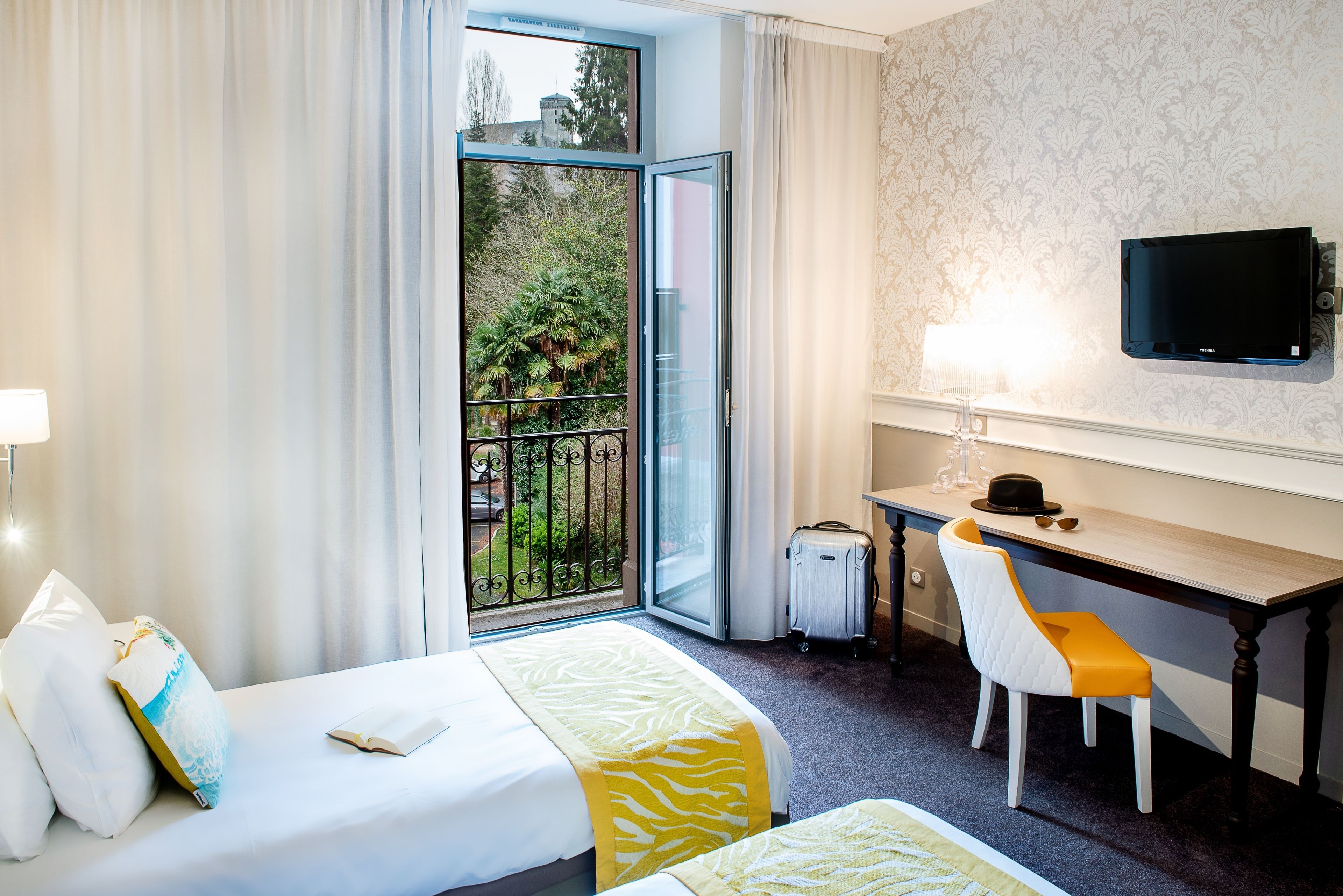 Habitación de hotel con dos camas, un escritorio, una silla, un televisor y vistas a zonas verdes a través de una puerta corredera.