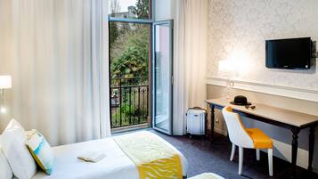 Habitación de hotel con dos camas, un escritorio, una silla, un televisor y vistas a zonas verdes a través de una puerta corredera.