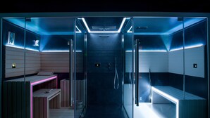 A modern, glass-walled sauna with a bench and a bench area, featuring a control panel and a shower. - Grand Hotel Gallia & Londres (Lourdes)