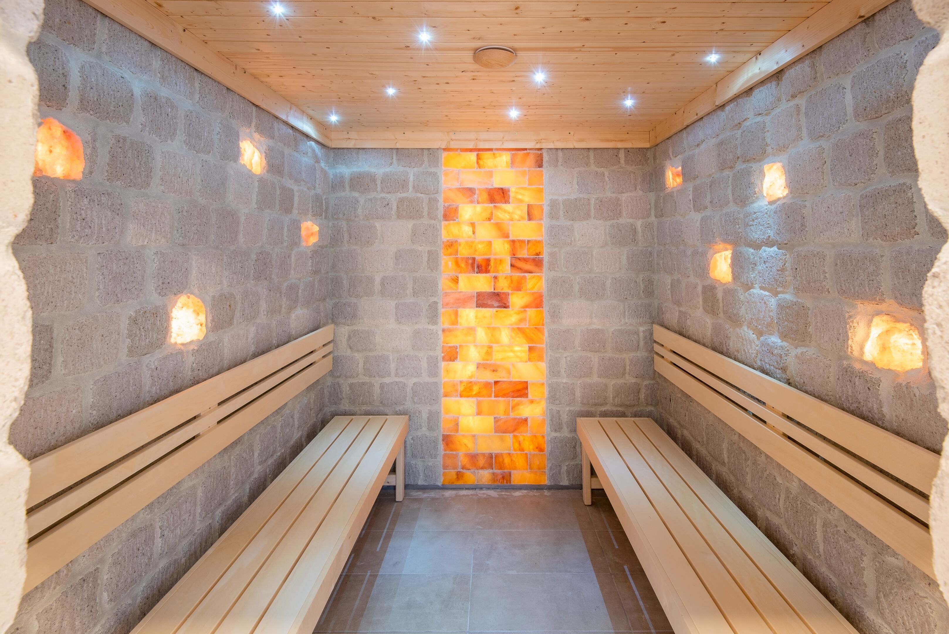 Una sauna con paredes de piedra, bancos de madera y una pared central calentada.