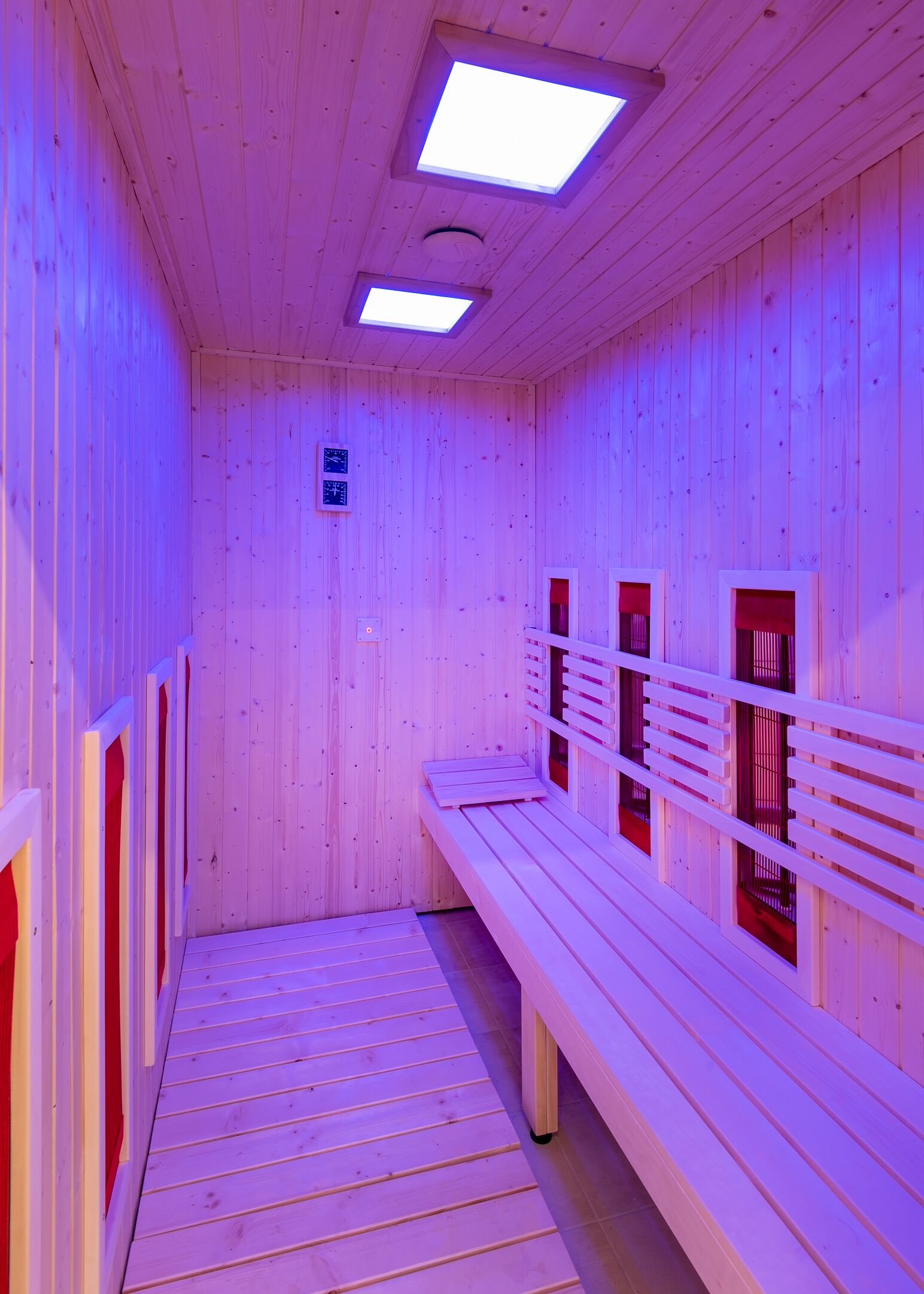 A sauna with wooden walls and benches, featuring skylights and a control panel.