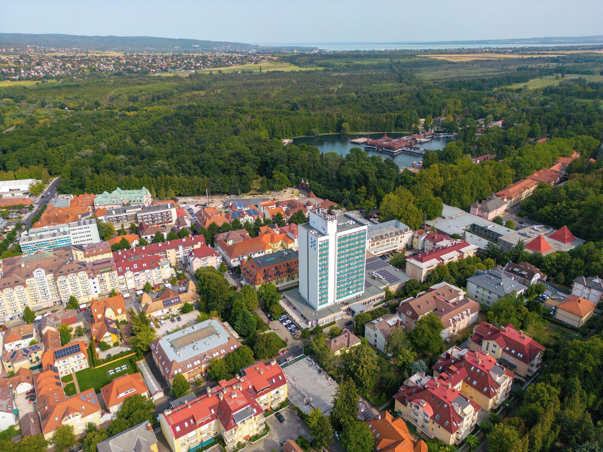 An aerial view of a town with a mix of residential and commercial buildings, including a prominent hotel with a modern design and a large parking area.