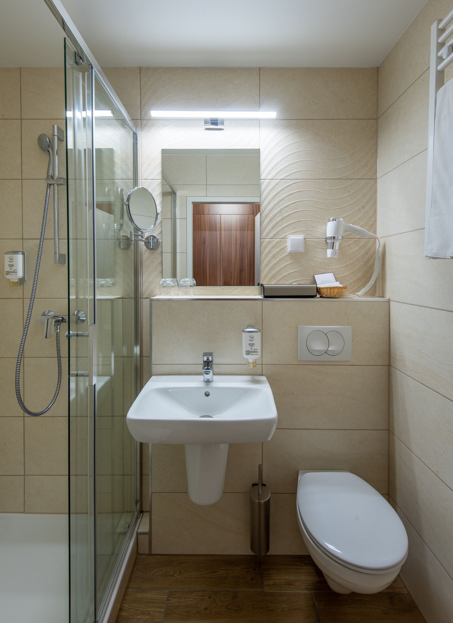 Un baño pequeño con cabina de ducha de vidrio, lavabo con espejo, inodoro y perchero.