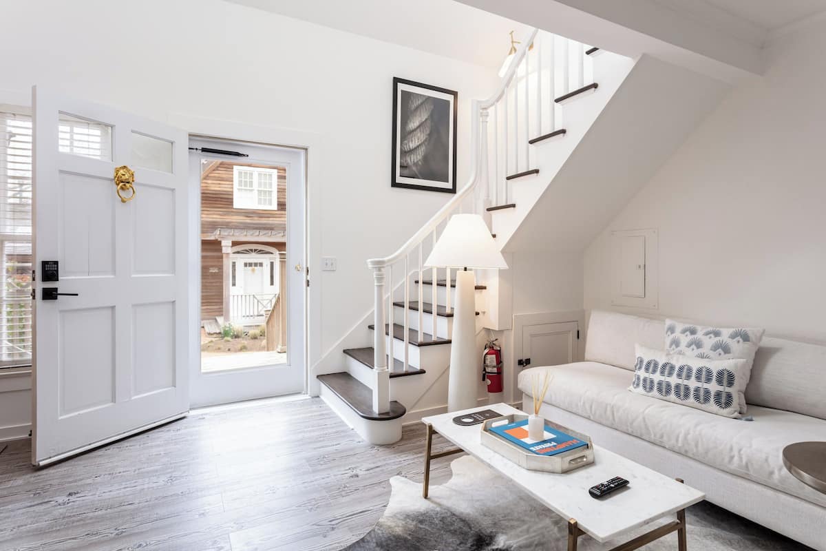 Uma sala de estar moderna com um sofá branco, uma mesa de centro e uma escadaria que leva a um andar superior.
