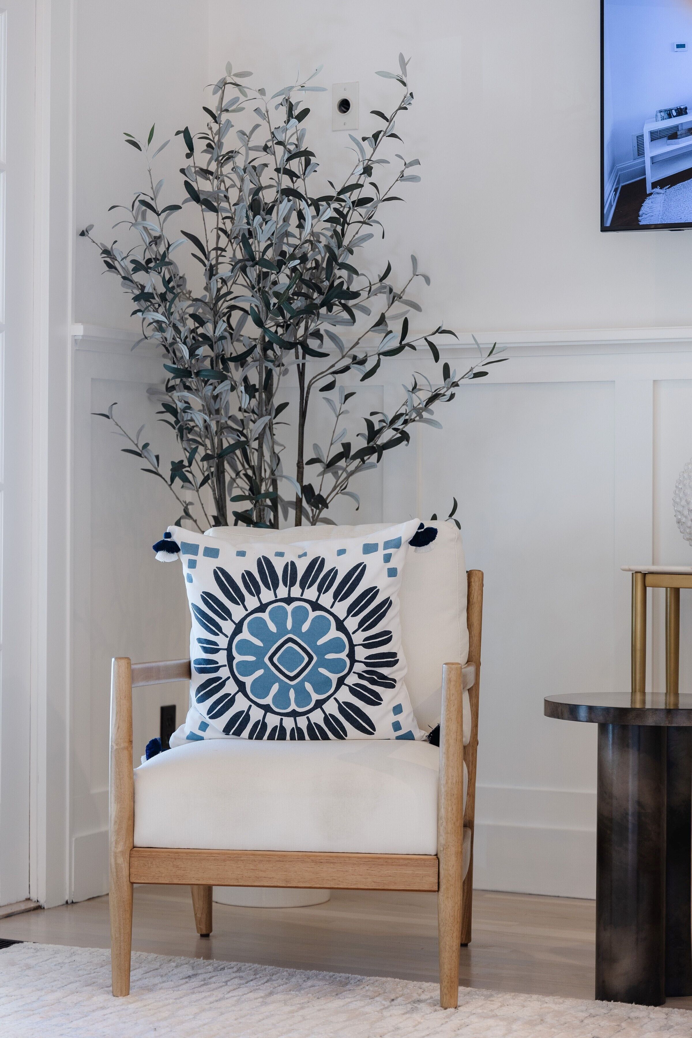 A chair with a decorative pillow, a small table, and a plant.