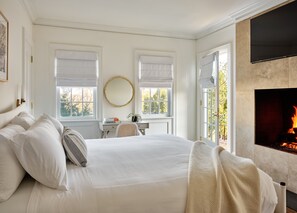Ein Schlafzimmer mit einem großen Bett, einem Schreibtisch, einem runden Spiegel und einem Kamin.