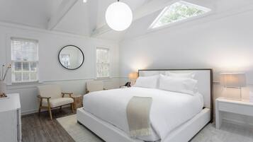 Quarto moderno com cama grande, mesas de cabeceira, espelho redondo e claraboia.