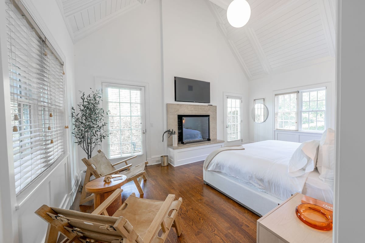 Um quarto espaçoso com uma cama grande, uma lareira, uma TV montada acima e vista para o exterior pelas janelas.