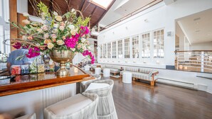 A spacious bar area with a large floral arrangement, seating with cushioned chairs, and a view of the upper level through large windows. - EHP Resort & Marina (East Hampton)