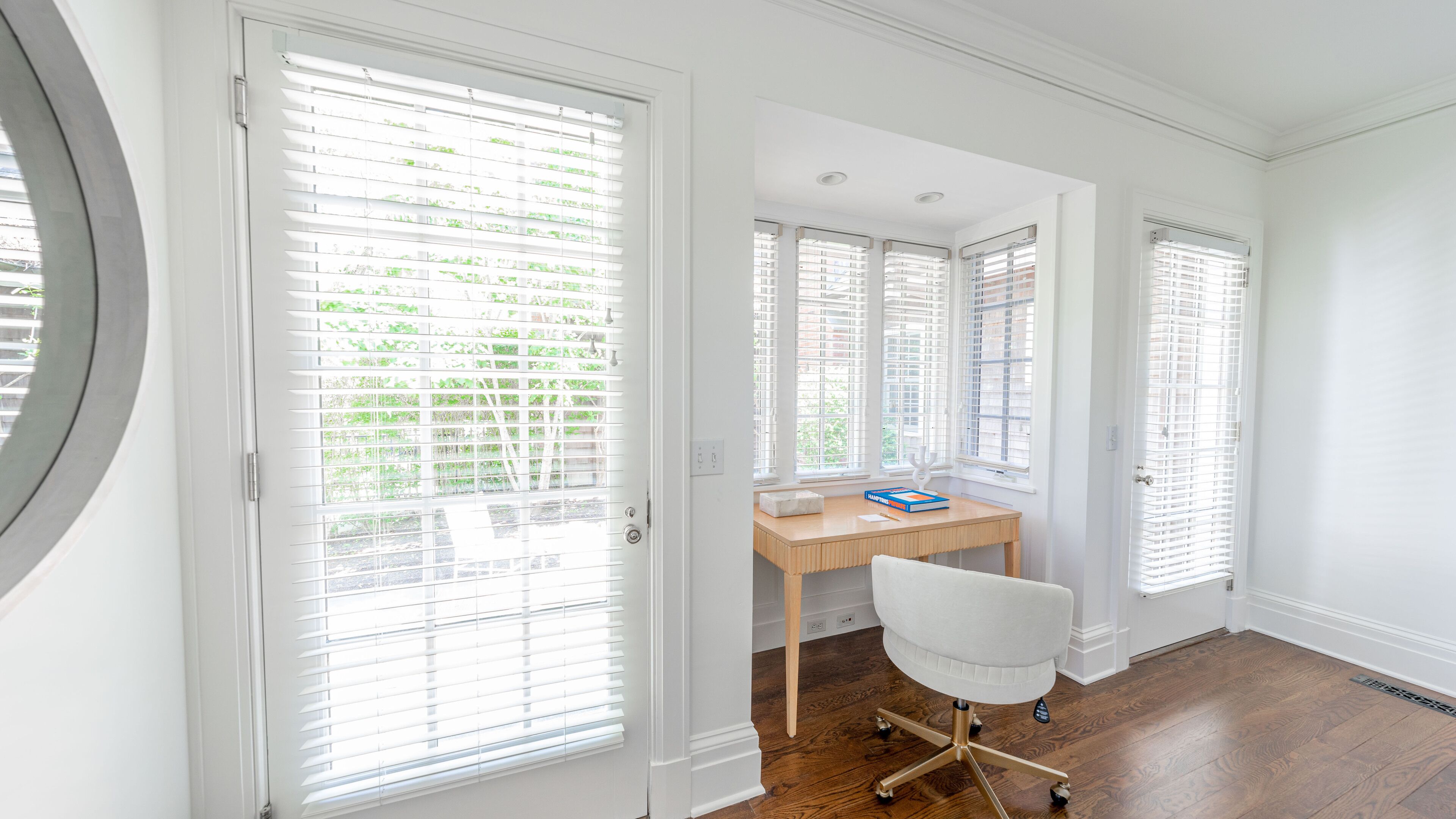 Una habitación con escritorio, silla y ventanas amplias con persianas.