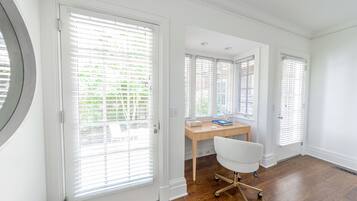 Una habitación con escritorio, silla y ventanas amplias con persianas.