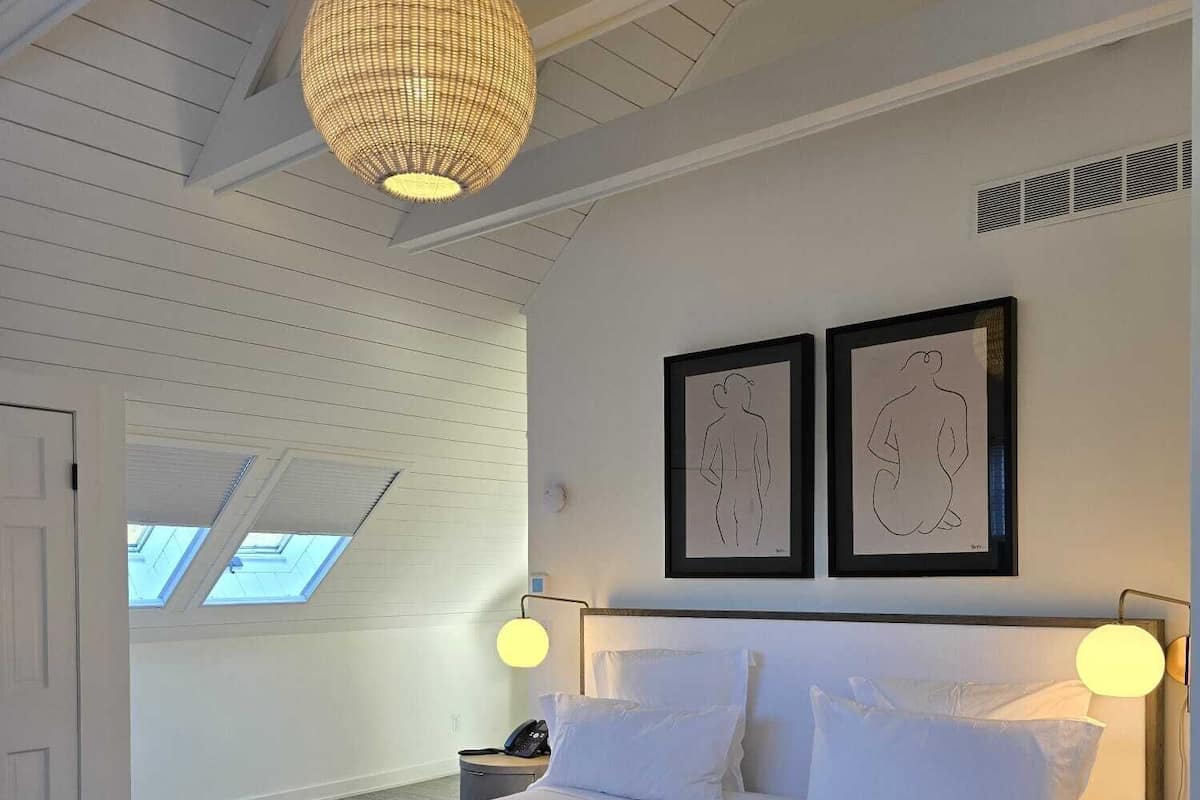 Quarto com uma cama grande, duas luminárias fixadas na parede e duas obras de arte emolduradas.