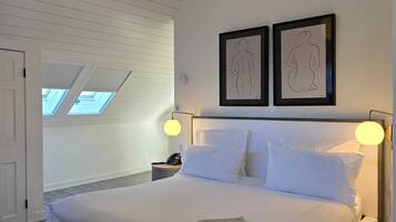 A bedroom with a large bed, two wall-mounted lamps, and two framed artworks.
