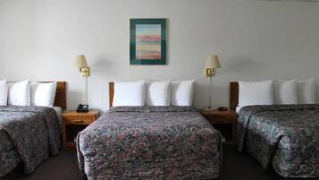 A hotel room with three beds, each with a patterned bedspread, a nightstand with a lamp, and a wall-mounted painting.
