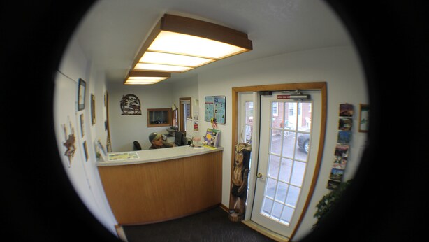 A reception area with a wooden counter, framed pictures on the wall, and a door leading outside. - Budget Host Crestview Inn (Sault Ste. Marie)