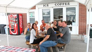 A group of people seated at wooden tables outside a coffee shop with a Coca-Cola vending machine. - Budget Host Crestview Inn (Sault Ste. Marie)