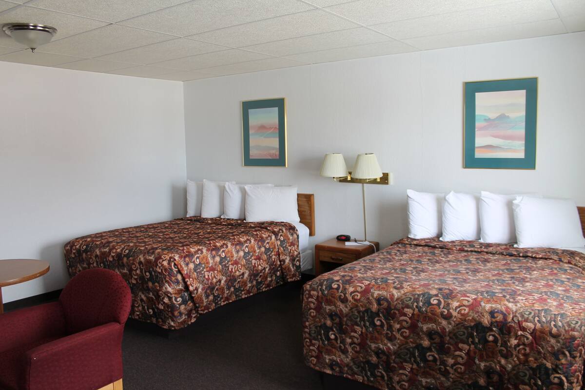 A hotel room with two beds, a small table, a chair, and two wall-mounted lamps.