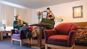 A hotel room with a seating area featuring two armchairs and a sofa, a small table, and a vase with flowers. - Budget Host Crestview Inn (Sault Ste. Marie)