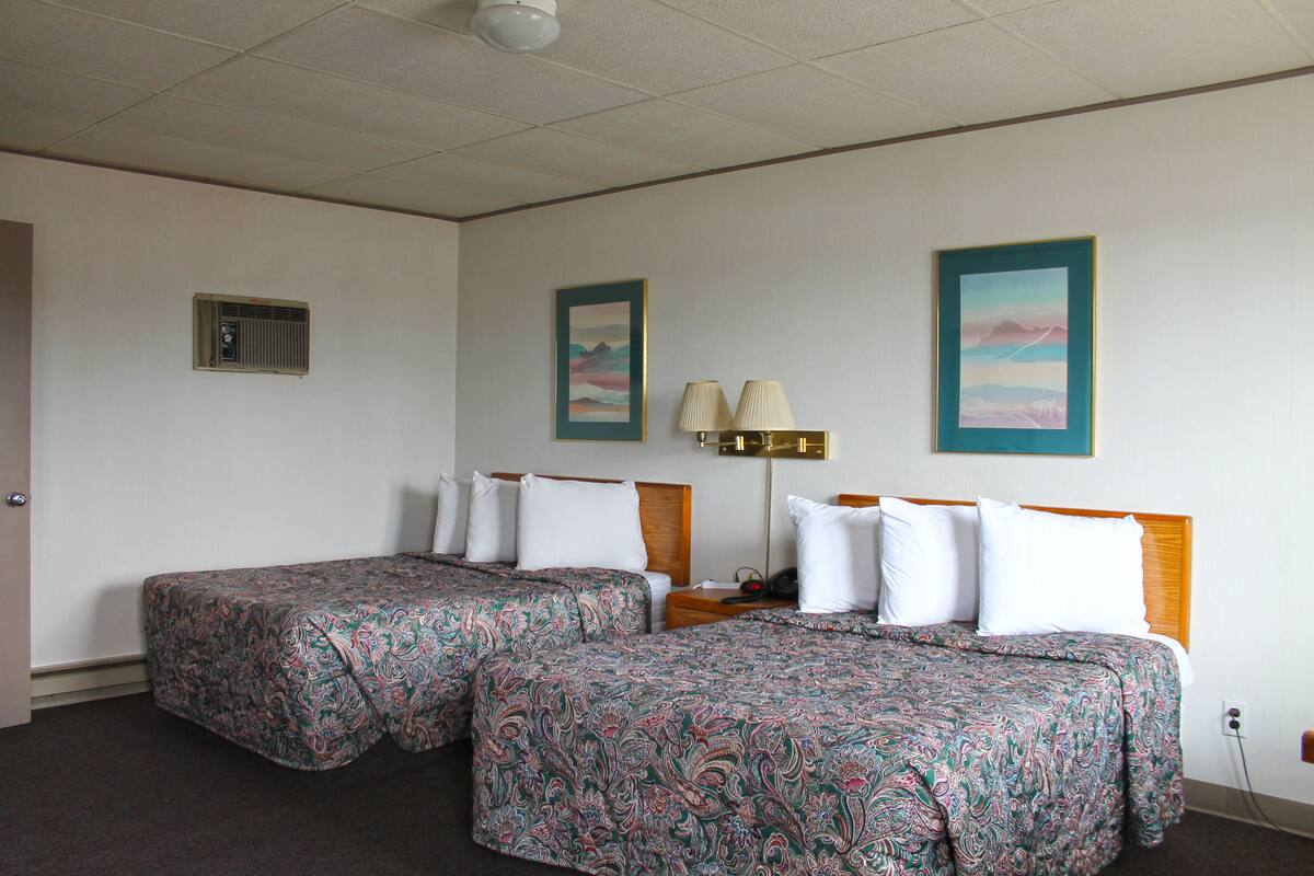 A hotel room with two beds, a nightstand, a lamp, and a painting on the wall.