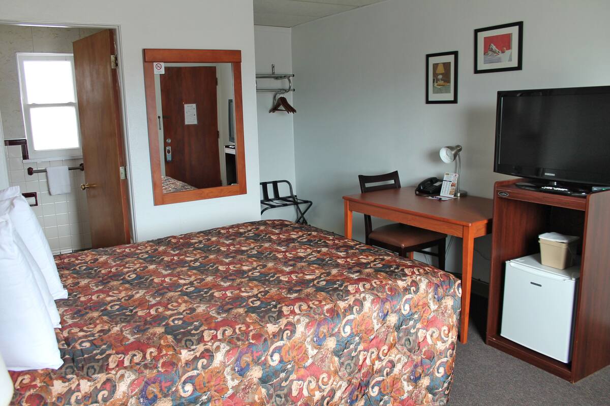 A hotel room with a bed, a desk with a chair, a television, and a refrigerator.