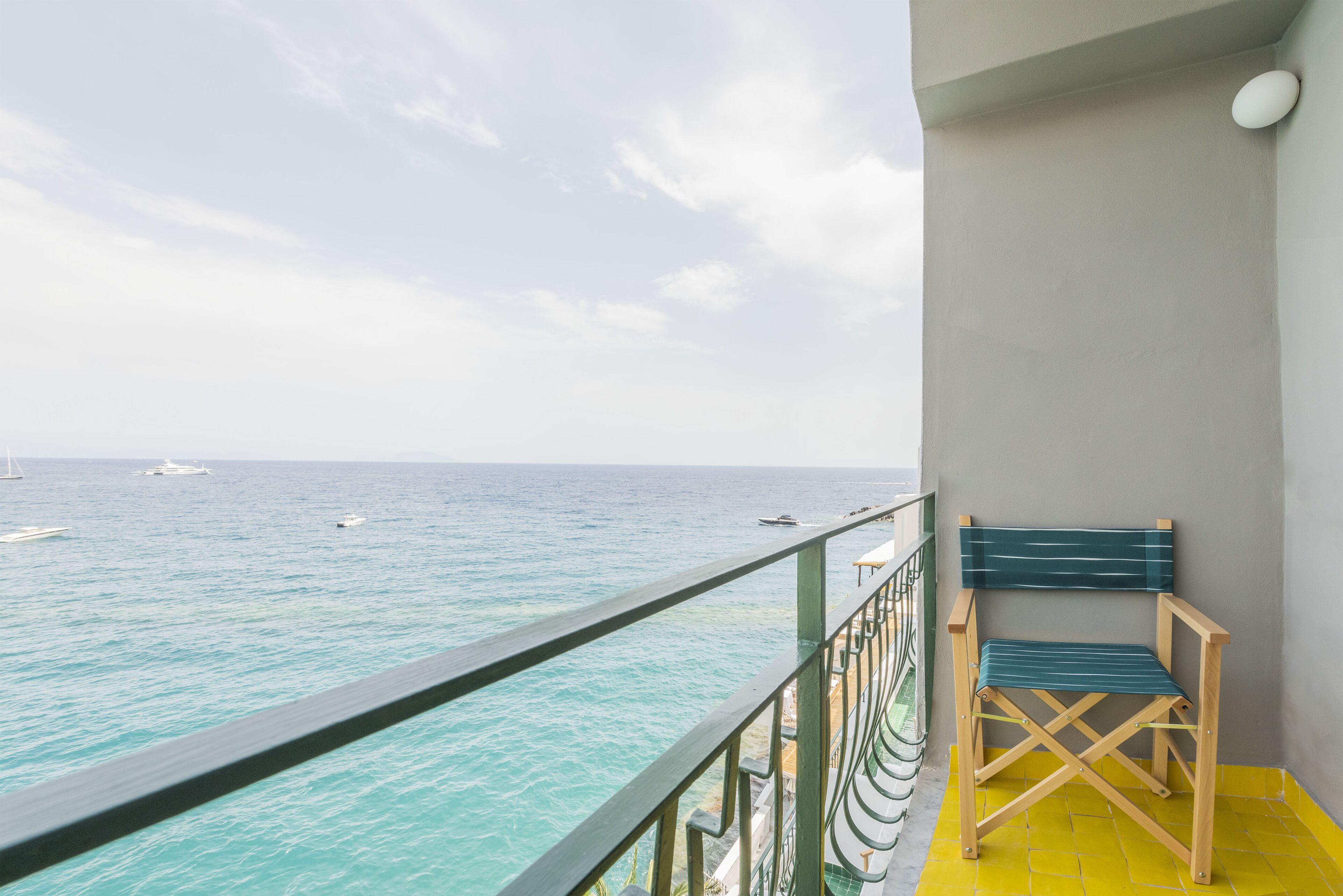 A balcony with a view of the sea, a chair, and a railing.