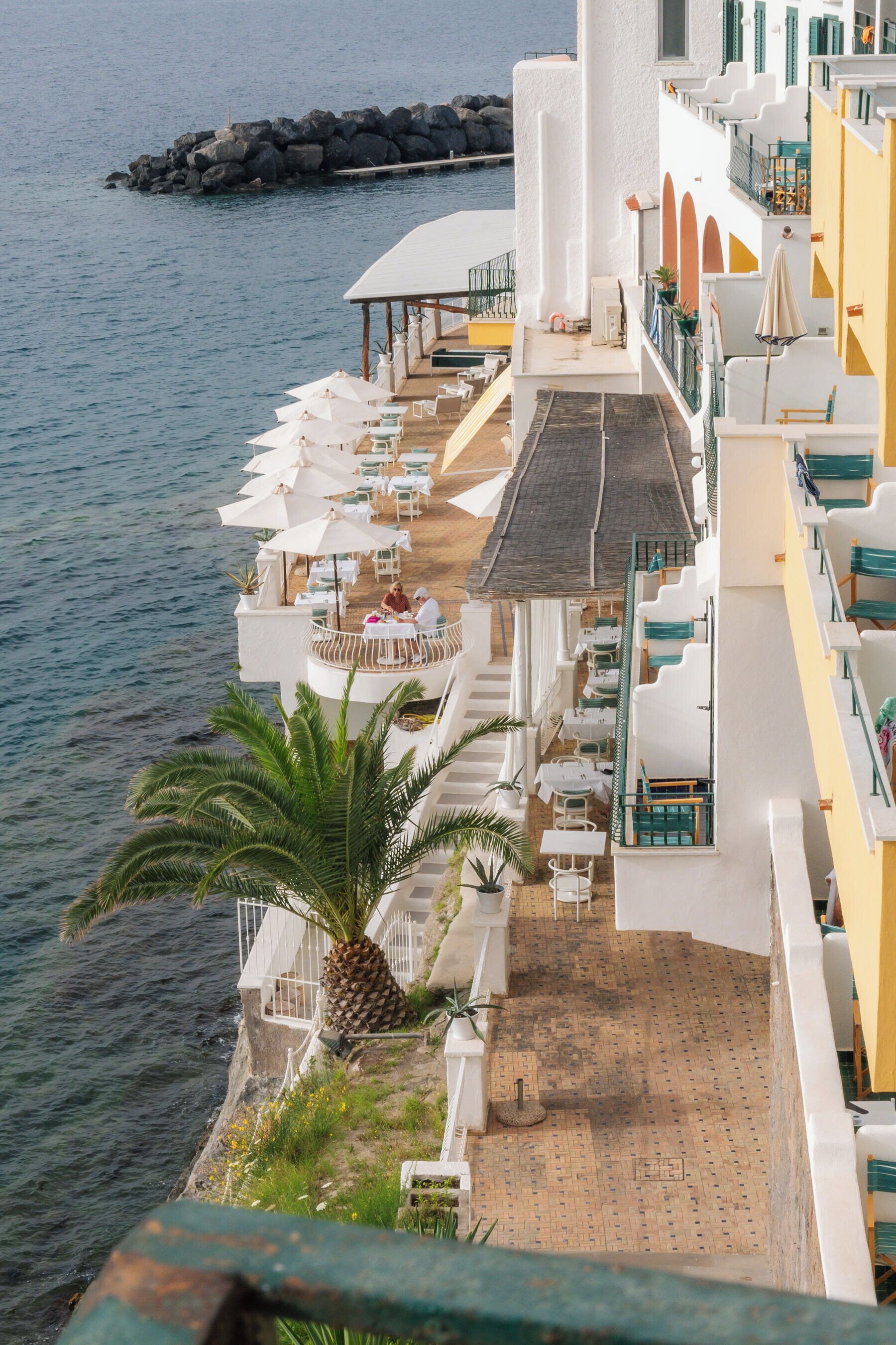 A seaside hotel with outdoor seating and a view of the sea.