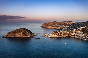 A coastal town with a prominent rocky island and a small sailboat in the water.