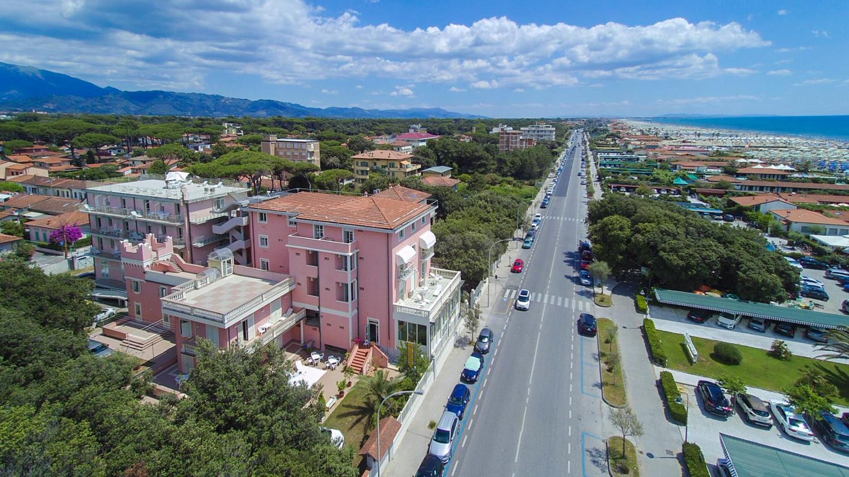 Vista aérea de un pueblo costero con un edificio rosa destacado, una calle principal y vistas al mar.