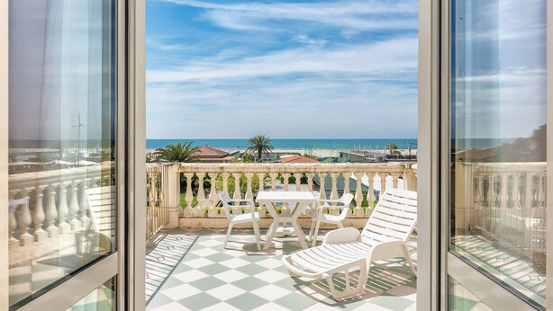 A balcony with a checkered floor, white chairs, and a table. - Happy Hotel (Pietrasanta)