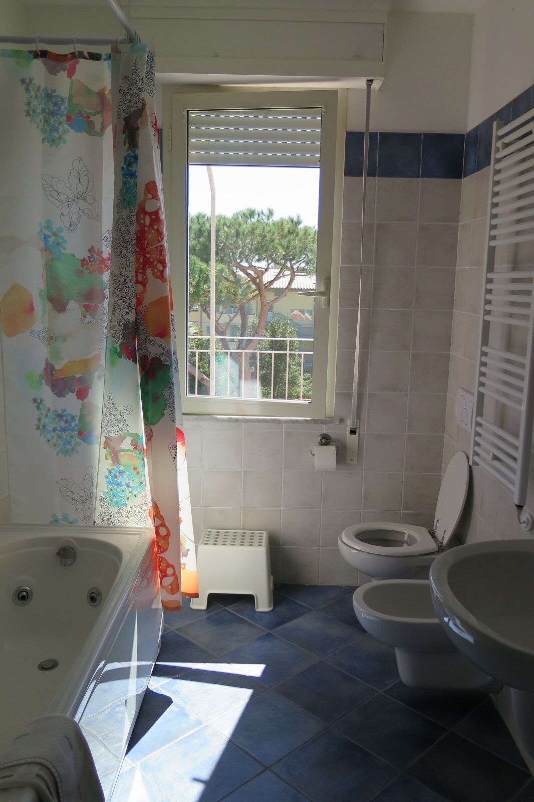 Un baño con bañera, inodoro y ventana con vistas a árboles.