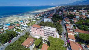 An aerial view of a coastal town with a beach, residential buildings, and a large hotel complex. - Happy Hotel (Pietrasanta)