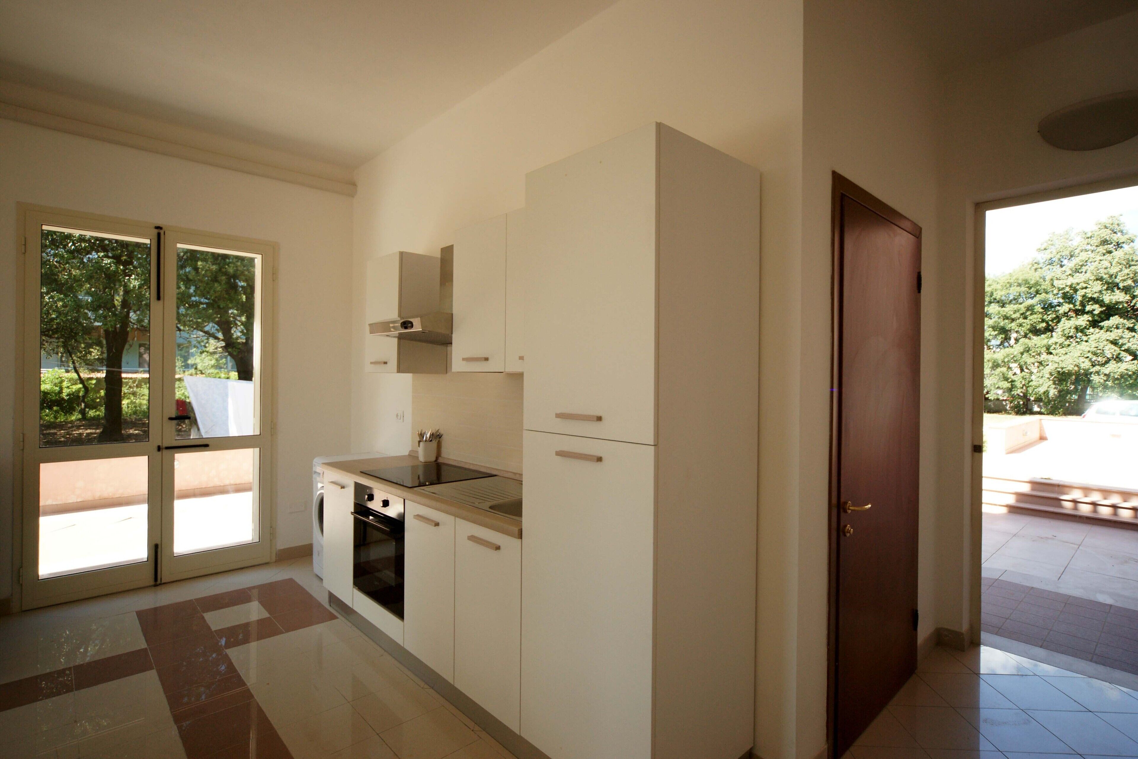 A modern kitchen with white cabinets, a built-in oven, and a window overlooking a garden.