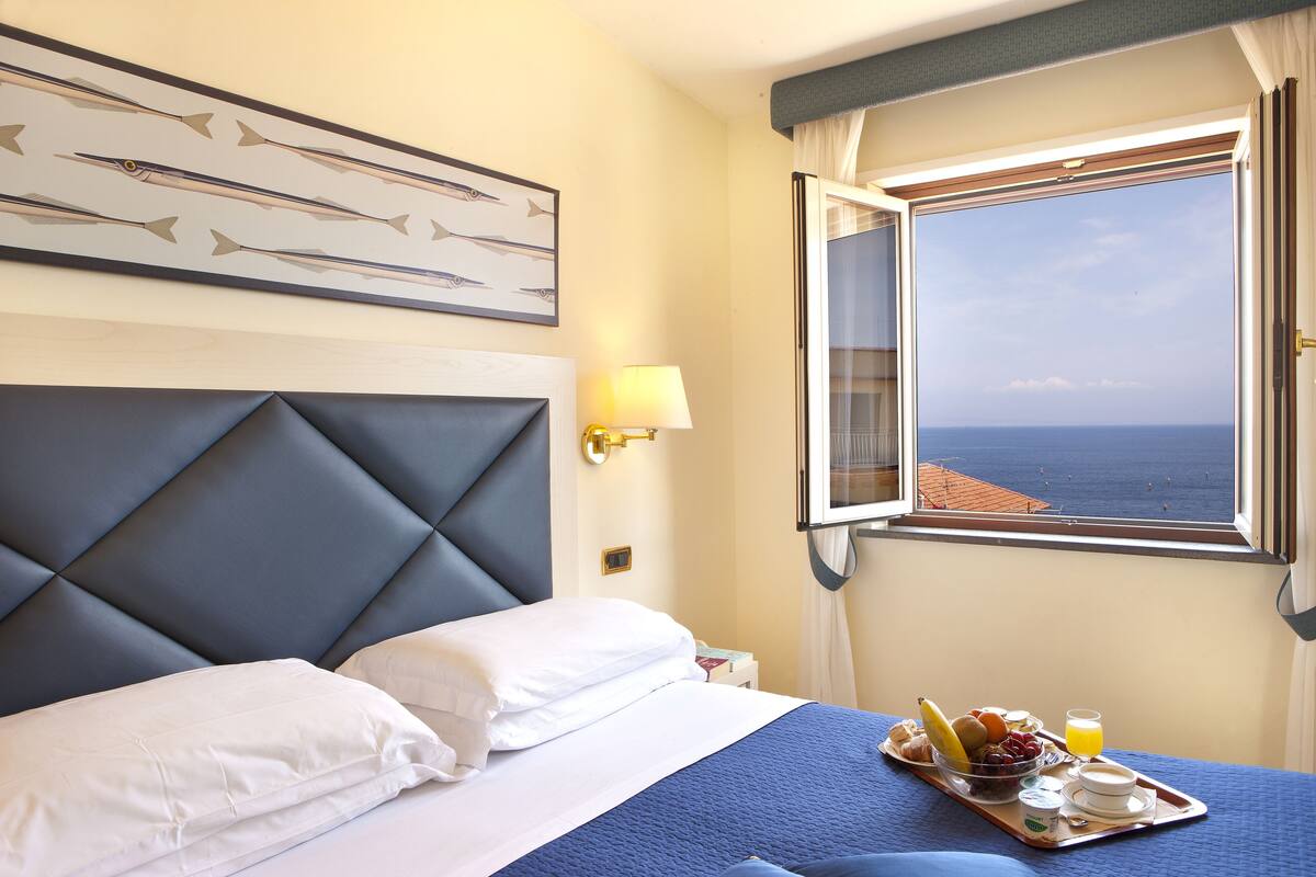 Habitación de hotel con una cama grande, vistas al mar y una bandeja de desayuno en la mesita de noche.