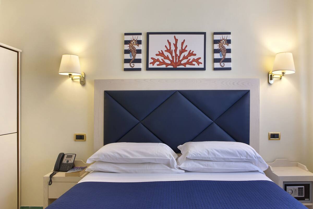 Una habitación de hotel con una cama grande, dos mesitas de noche, un teléfono y cuadros en la pared.