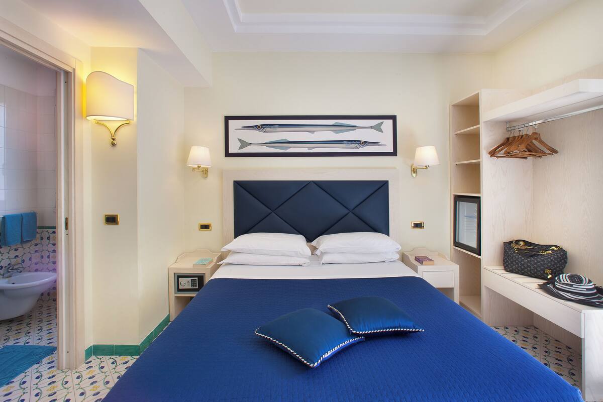 Una habitación de hotel con cama, mesitas de noche, un armario para abrigos y un baño.