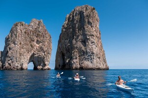 Kayakisti su un mare calmo, con ampie formazioni rocciose sullo sfondo.