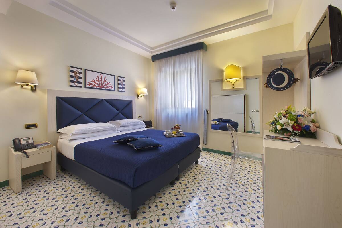 Habitación de hotel con una cama grande, mesitas de noche, un escritorio, un espejo y un suelo estampado.