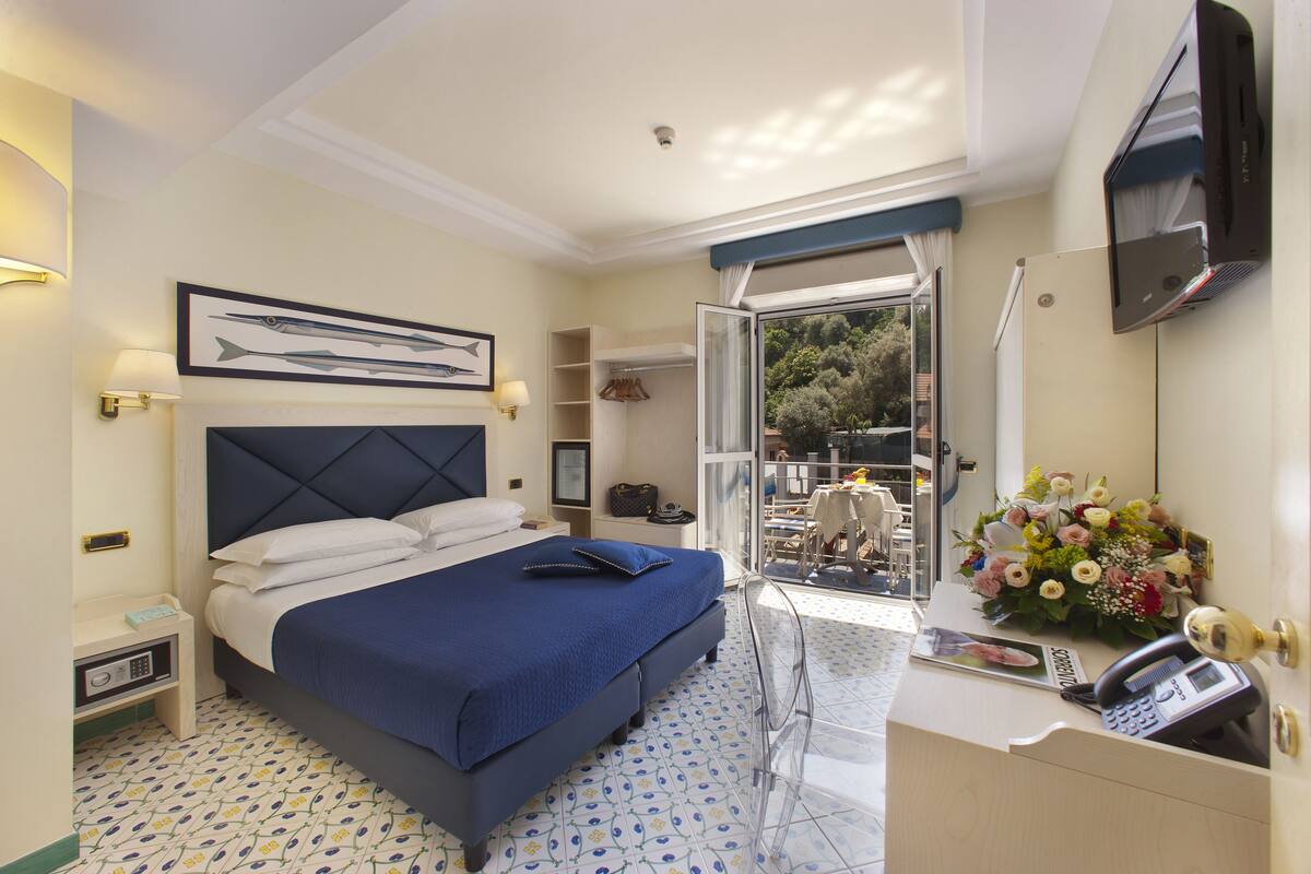 Habitación de hotel con cama, mesita de noche, escritorio, silla y vistas al exterior.