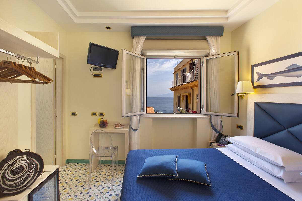 Habitación de hotel con cama, televisor, ventana con vista a edificios y baño con ducha.